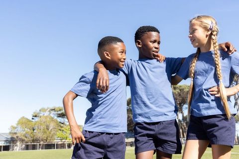 Kids linking arms on school field smiling teamwork in blue tees and navy shorts