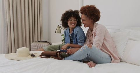 African American Friends Packing Carry-On Luggage on Bed Smiling While Holding Passport