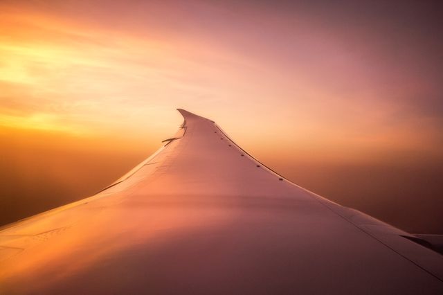 Airplane wing reflecting orange and pink colors of sunset. Perfect for travel blogs, aviation articles, advertisements for airlines or travel agencies. Captures beautiful moments of flight during sundown.