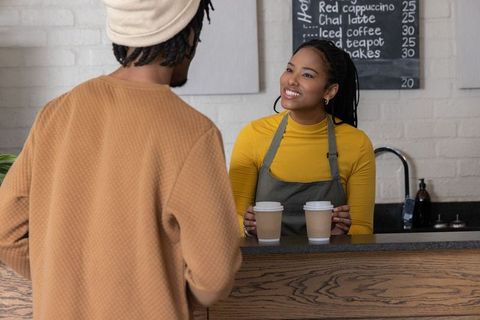 Smiling african american barista serving two takeout coffee cups at warm wood cafe counter