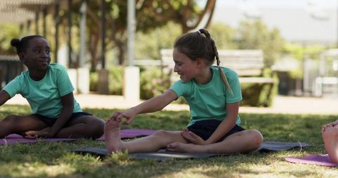 Teen girls stretching on mats in park during outdoor fitness class and school yoga