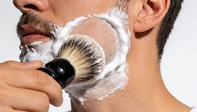 Applying thick shaving lather with brush on male stubble closeup for grooming