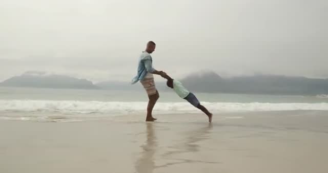 African American father and young son enjoying quality time on beach, with father spinning child around. Ideal for use in advertisements, family lifestyle blogs, parenting articles, travel brochures, and summer promotions highlighting outdoor fun and familial bonding.