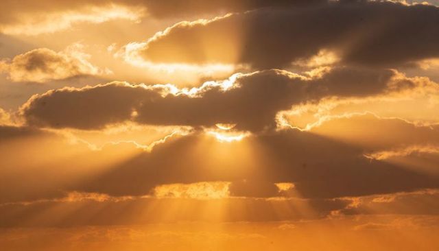 Sun casting golden crepuscular rays through layered clouds at serene dawn horizon glow