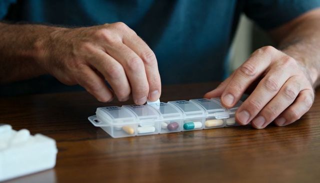 Sorting medications into clear weekly pill organizer, adult man managing daily pill routine