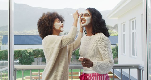 Happy diverse female friends applying beauty face mask at balcony. spending quality time at home.