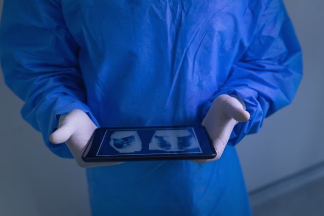 Mid section of male surgeon examining x-ray report on digital tablet in operating room at hospital