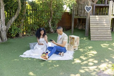 Couple celebrating engagement during backyard picnic showing ring and smartphone
