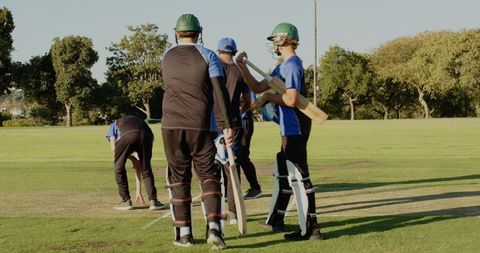 Youth cricket team preparing for batting drill on sunny grass pitch with helmets and pads