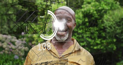 Smiling senior man wearing kufi and beaded necklace with futuristic hud overlay in garden