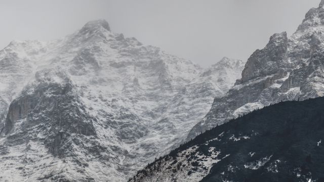 Snow-covered mountain peaks with steep, rugged slopes, shrouded in foggy weather. Ideal for use in travel publications, nature photography collections, environmental awareness campaigns, or scenic backgrounds for digital and print media.