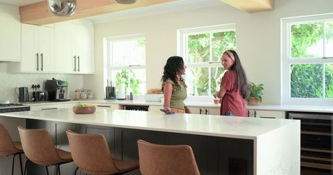 Two Women Chatting at Marble Kitchen Island Holding Smartphone and Fruit Bowl