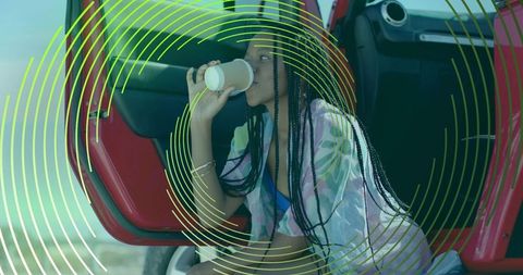 Woman relaxing coastal getaway with beverage by red suv