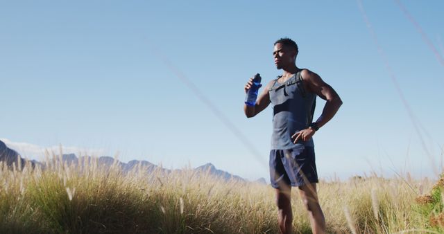 African american man exercising outdoors drinking water in countryside on a coast. fitness training and healthy outdoor lifestyle.