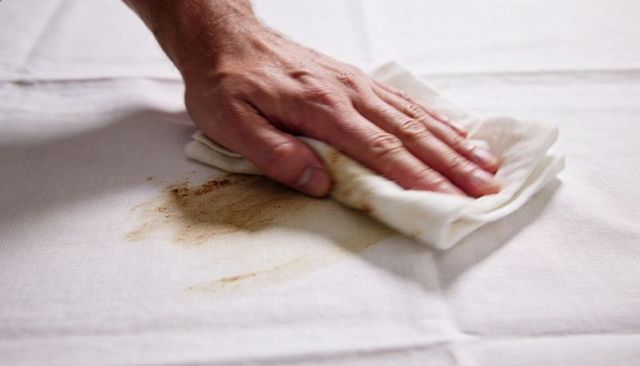 Hand wiping brown stain from white tablecloth with cloth closeup cleaning action