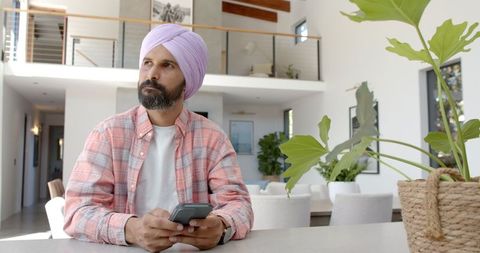 Concentrated Indian Man in Turban Using Smartphone at Home