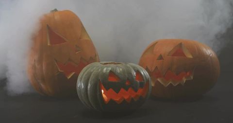 Glowing carved jack-o'-lanterns sitting on dark table with drifting fog