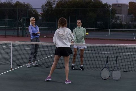 Women practicing tennis at dusk on outdoor court for training, teamwork, and drills