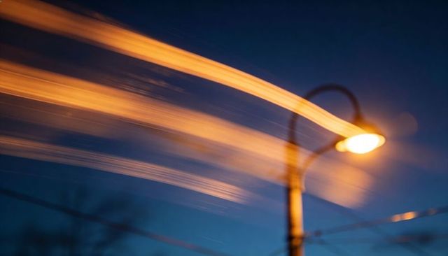 Glowing street lamp casting amber light trails across night sky long exposure urban bokeh