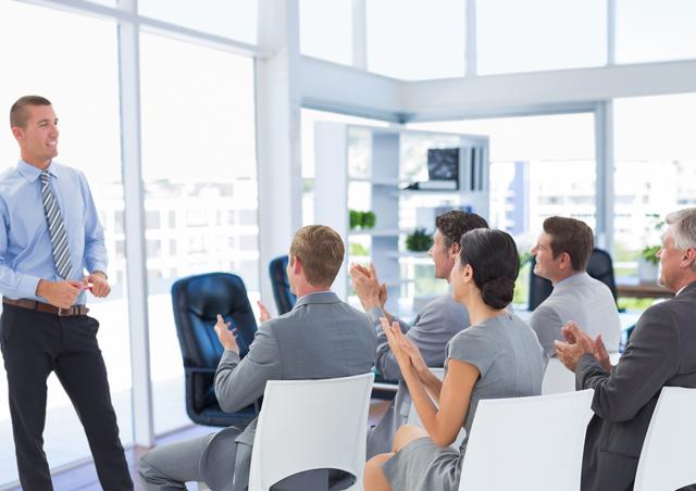 Business executives are seen applauding a colleague's presentation in a modern conference room. This image is ideal for illustrating concepts related to corporate meetings, teamwork, professional development, and business success. It can be used in business blogs, corporate websites, training materials, and presentations.
