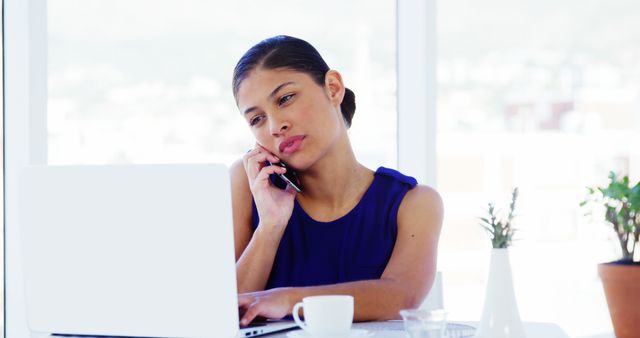 Focused Businesswoman Talking on Phone and Working on Laptop in Modern Office - Download Free Stock Images Pikwizard.com