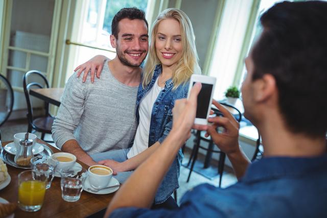 Friend clicking photos of couple from mobile phone in cafÃ©