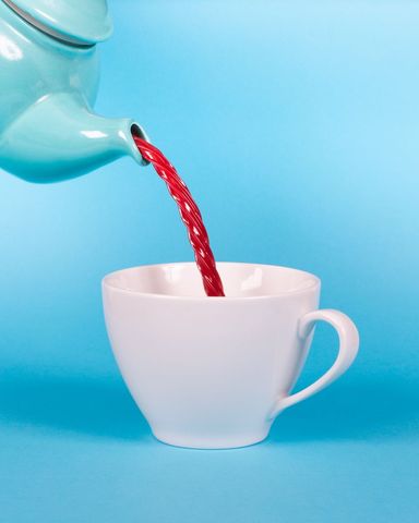 Conceptual tea time with red licorice twist pouring into mug