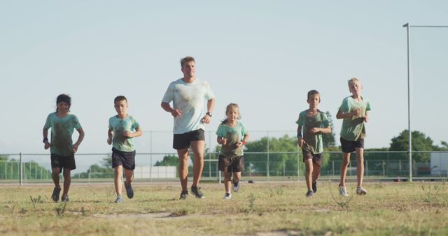 Children running with coach outdoors on a sunny day during summer. Ideal for promoting youth sports programs, health and fitness initiatives, teamwork, and outdoor activities for kids. Suitable for use in advertisements, brochures, and educational materials focusing on youth athletic programs and healthy living.