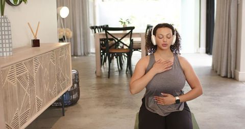 Woman practicing mindful breathing at home wearing headphones and smartwatch