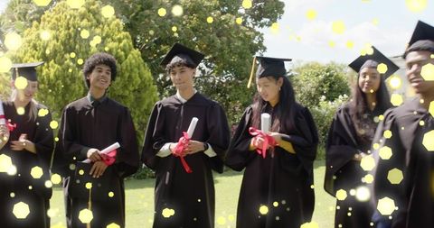 Graduates celebrating outdoors holding red-ribbon diplomas in black gowns