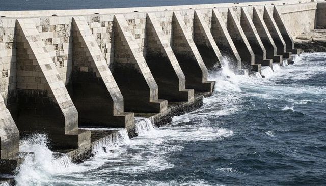 Diagonal stone seawall with repetitive piers and crashing waves, coastal breakwater texture