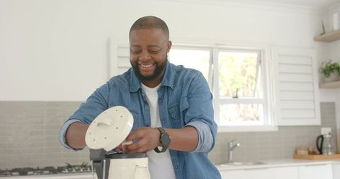 African man assembling blender and smiling in bright modern kitchen, home appliance use