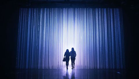 Silhouetted Figures Walking Through Vertical LED Light Curtain in Contemporary Gallery
