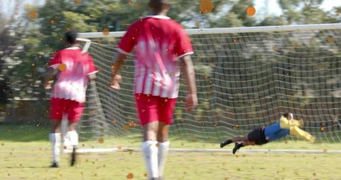 Diving goalkeeper making key save at goal while teammates sprinting back on soccer pitch