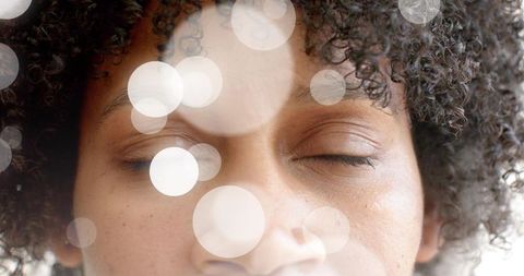 Closeup relaxing mid adult woman with curly hair, eyes closed, soft bokeh light and skin texture