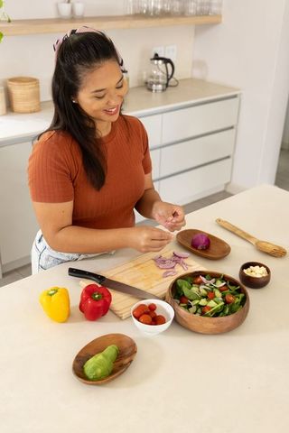 Mid-adult asian woman preparing fresh vegetable salad on modern minimal kitchen countertop