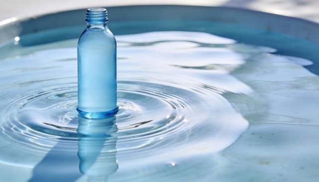 Translucent blue bottle floating and creating concentric ripples on calm water surface