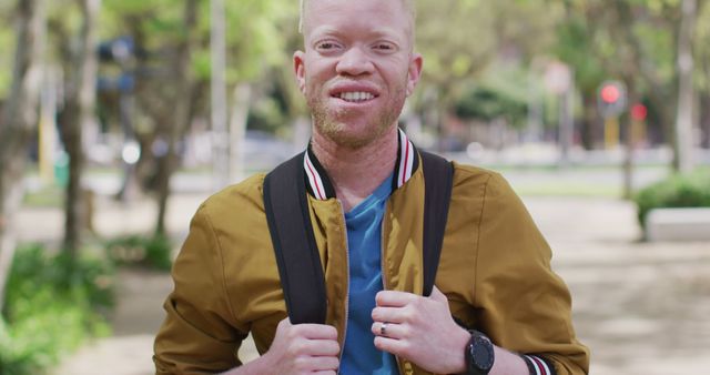 Portrait of smiling albino african american man with dreadlocks in park looking at camera. on the go, out and about in the city.