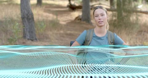 Woman hiker wearing teal tee carrying backpack on pine trail with turquoise grid overlay