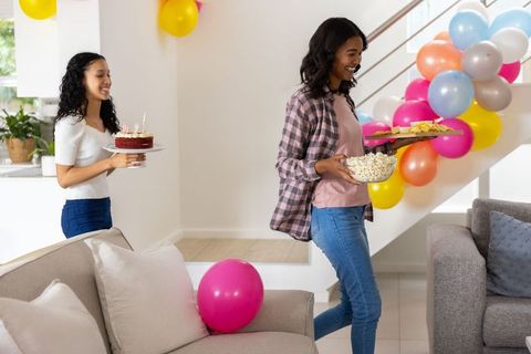 African american mom and teen daughter celebrating birthday with cake, balloons and snacks
