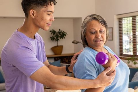 Senior exercising with trainer's support at home for safe rehabilitation