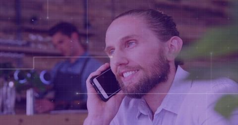 Bearded man talking on smartphone at cafe counter while barista preparing espresso