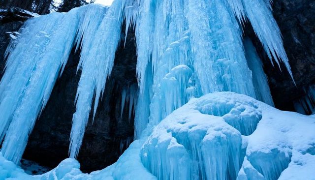 Frozen waterfall cascading down dark cliff with dramatic blue icicles and snow formations