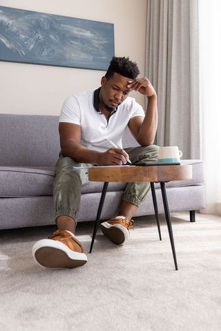 African american man writing in notebook on coffee table, contemplative home workspace