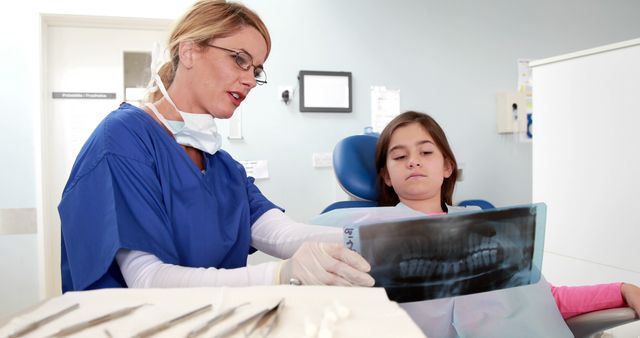A Caucasian female dentist is showing a young girl her dental X-ray, with copy space. They are in a dental clinic, where the dentist is explaining the diagnosis or treatment plan to her patient.
