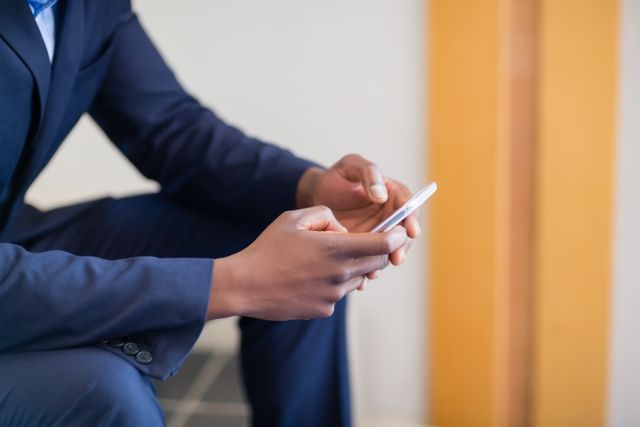 Businessman in a suit using a mobile phone, focusing on hands and device. Ideal for illustrating concepts of business communication, technology in the workplace, professional networking, and modern corporate environments.