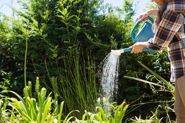 Woman watering plants with watering can in garden on a sunny day