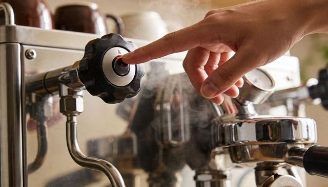 Hand pressing steam knob on commercial espresso machine releasing steam over portafilter