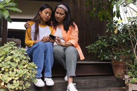 Mother and Teen Daughter Bonding Outdoors Browsing Phone