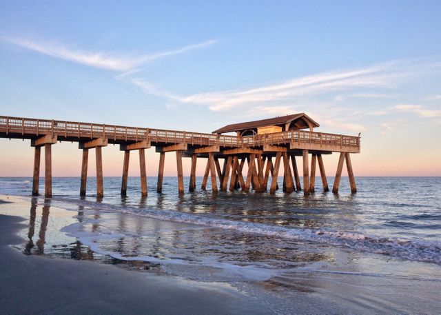 Serene scene of wooden pier extending over ocean during sunset with gentle waves and clear sky. Perfect for travel promotions, relaxation theme, scenic backgrounds, summer holiday ideas, and lifestyle inspiration. Evokes feelings of calmness and peace, ideal for brochures, websites, and social media content.